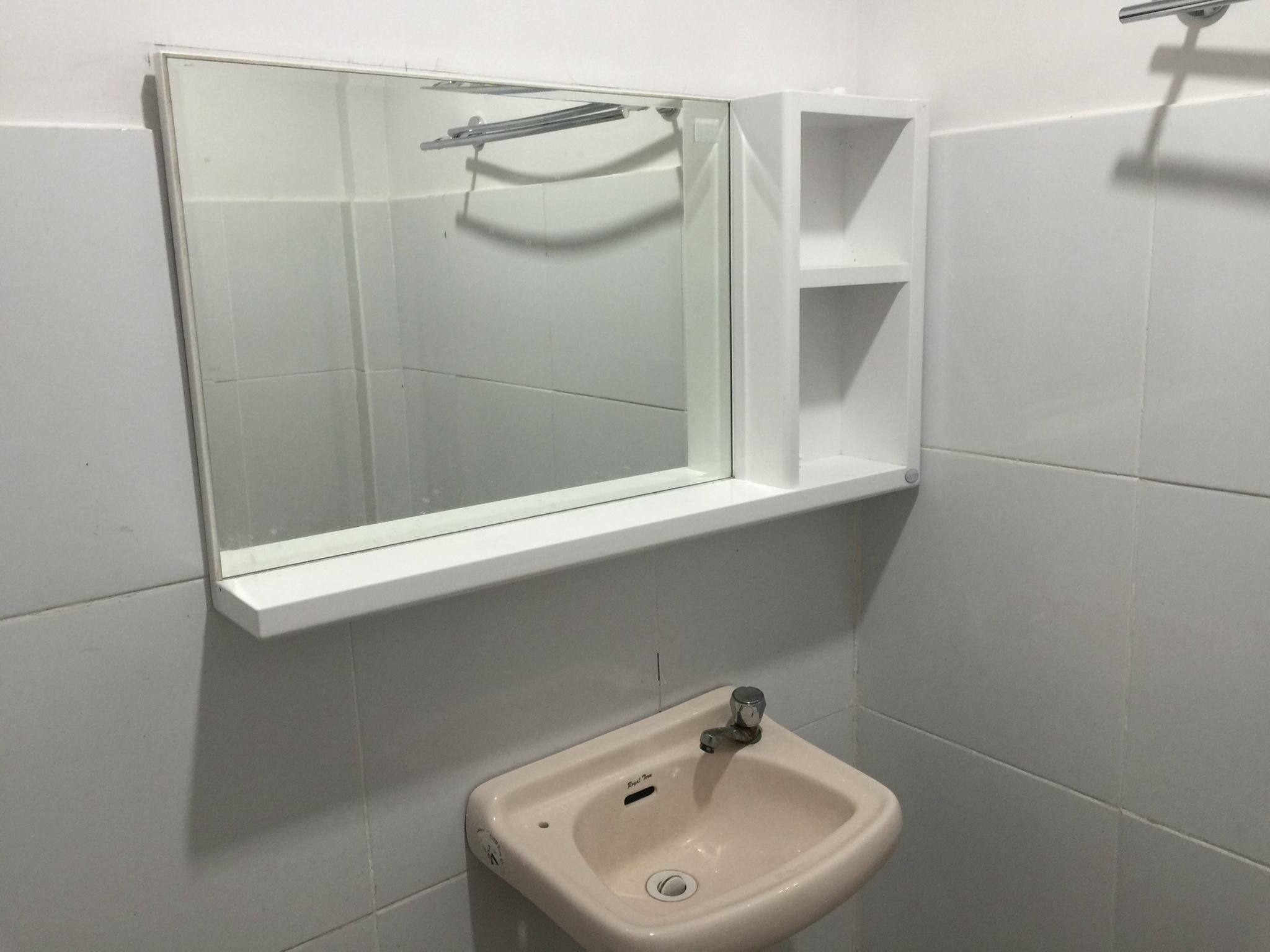 Une salle de bain avec un lavabo blanc, un miroir et une étagère au-dessus du lavabo.