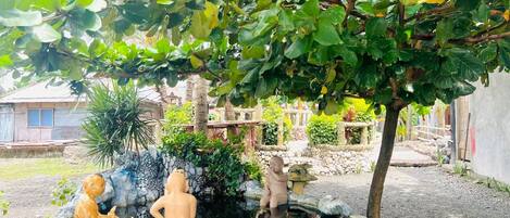 A garden with a stone fountain, three statues, and a variety of plants.