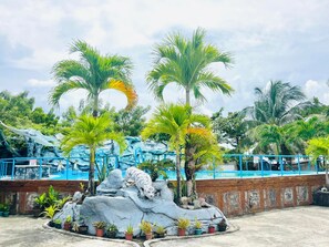 A tropical garden with palm trees, a rock formation, and a pool area. - Precia Villavert Beach Resort (San Jose de Buenavista)