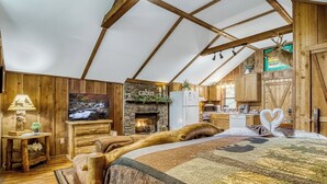 Interior rústico de una cabaña con chimenea, muebles de madera, televisor y una zona de cocina.