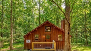 Une cabane en bois avec un porche à l’avant, une porte ornée d’une guirlande et un panneau indiquant qu’il s’agit d’un terrain de camping.