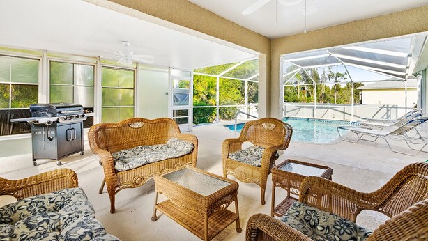 Un espace extérieur abrité, aménagé avec des meubles en osier, un barbecue et une piscine.