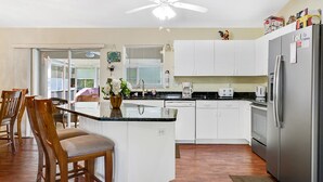 Une cuisine moderne avec des armoires blanches, un réfrigérateur en acier inoxydable, un four encastré et un ventilateur de plafond.