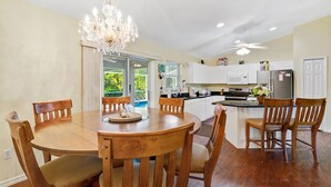 Un espace repas comprenant une table et des chaises en bois, un lustre et une vue sur l’extérieur.