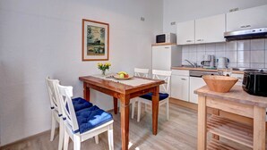 A compact kitchen with white cabinets, a wooden table, and a dining area with white chairs. - Villa Ostseewarte Whg. 6, TERRASSE - Villa Ostseewarte, STRANDNAH, teilw. (Heringsdorf)