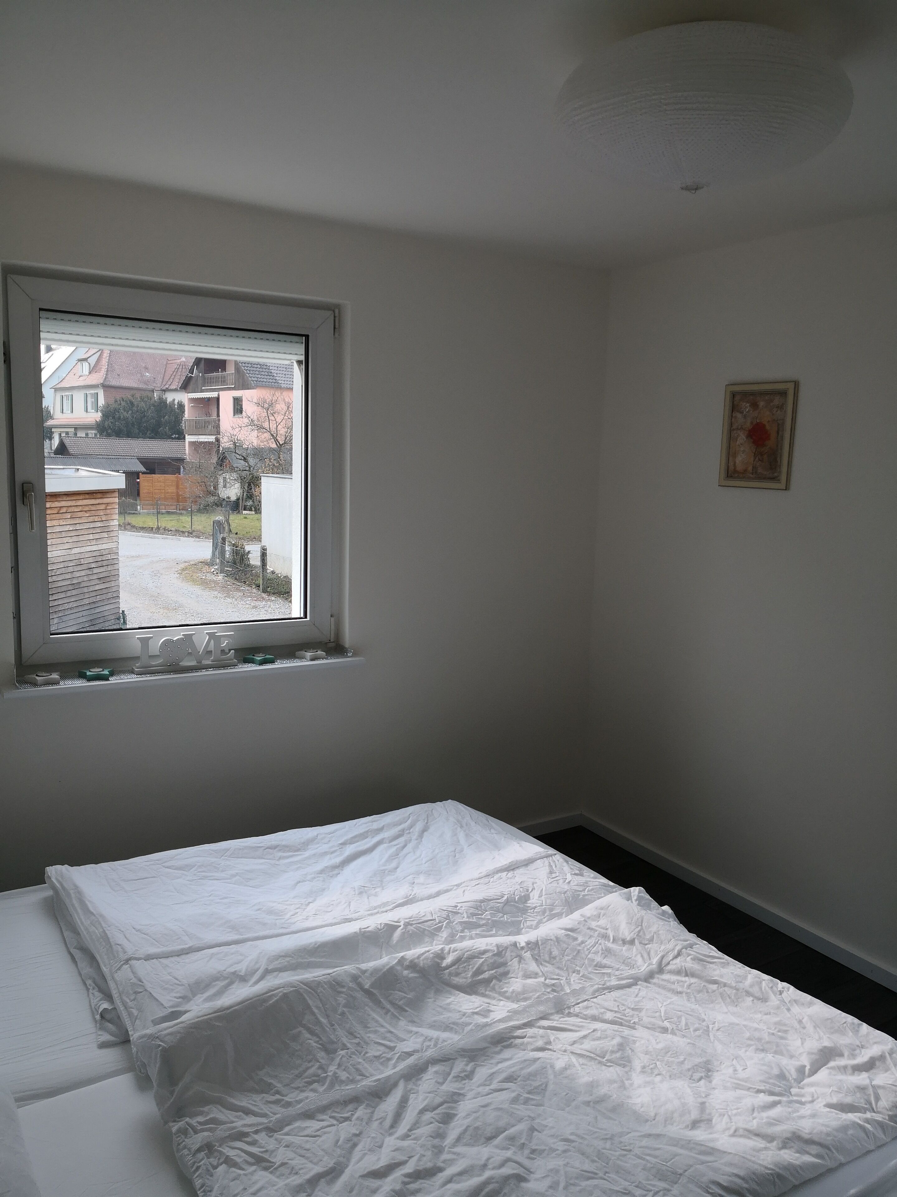 Une chambre avec un lit simple, une fenêtre et un tableau encadré au mur.