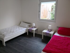 Une petite pièce propre, avec un lit, une table de chevet, une table et une fenêtre.