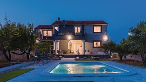 A two-story house with a swimming pool, outdoor seating, and a well-maintained garden.