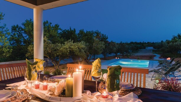An outdoor dining area with a pool in the background, tables set with candles and glassware.