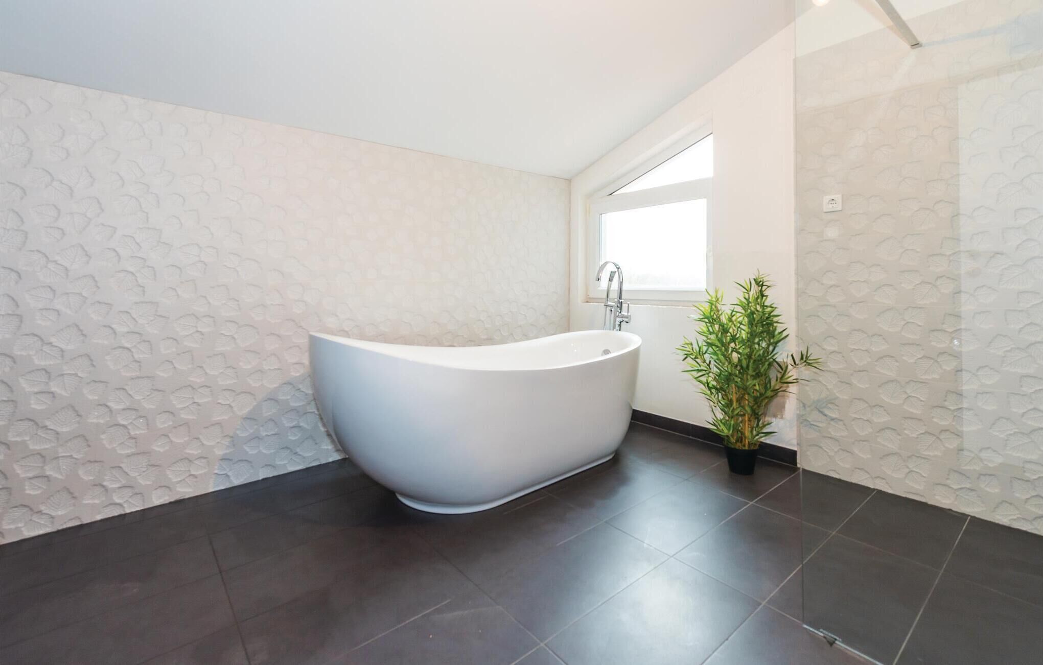 Un baño moderno con una bañera independiente, un ventanal y una planta en maceta.