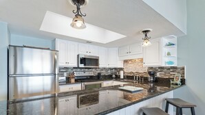 Una cocina moderna con una isla central, electrodomésticos de acero inoxidable e iluminación colgante.