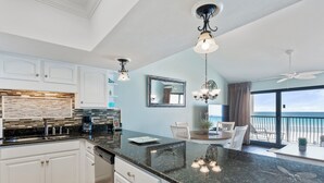 Una cocina moderna con armarios blancos, encimera de granito y un comedor con vistas al océano.