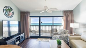 Una sala de estar con televisor, ventilador de techo, sofá, mesa de centro y vista a la playa.