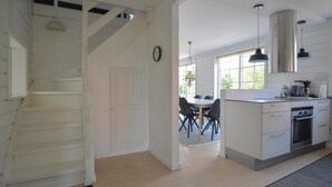 A modern kitchen with white cabinetry, a built-in oven, and a dining area with a table and chairs.