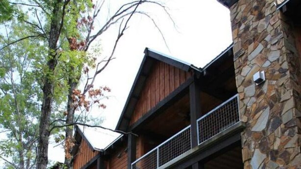 Un edificio de varios pisos con fachada de piedra y madera, balcones y mobiliario exterior.