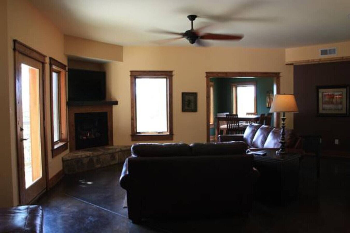 Una sala de estar con chimenea, ventilador de techo y vistas a través de un ventanal abierto.