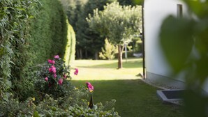 A garden with a hedge, pink flowers, and a view of a house with a wooden exterior. - Appartementhaus Weber (Arrach)