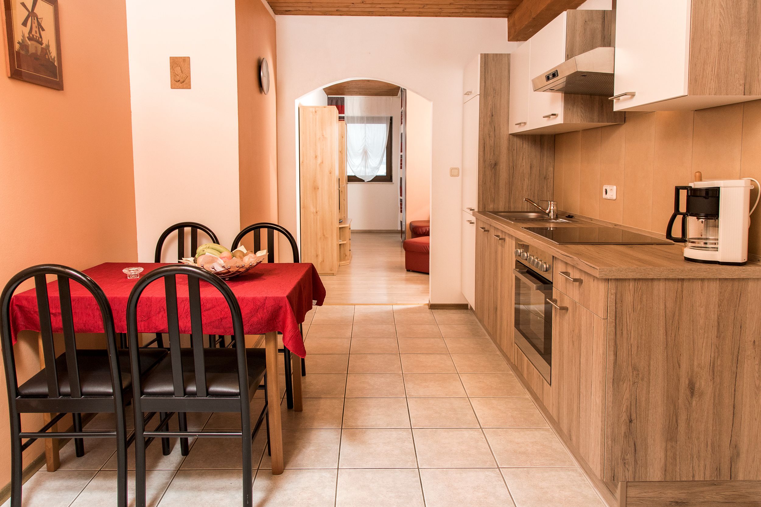A kitchen with wooden cabinets, a coffee maker, and a dining area with a red table and chairs.