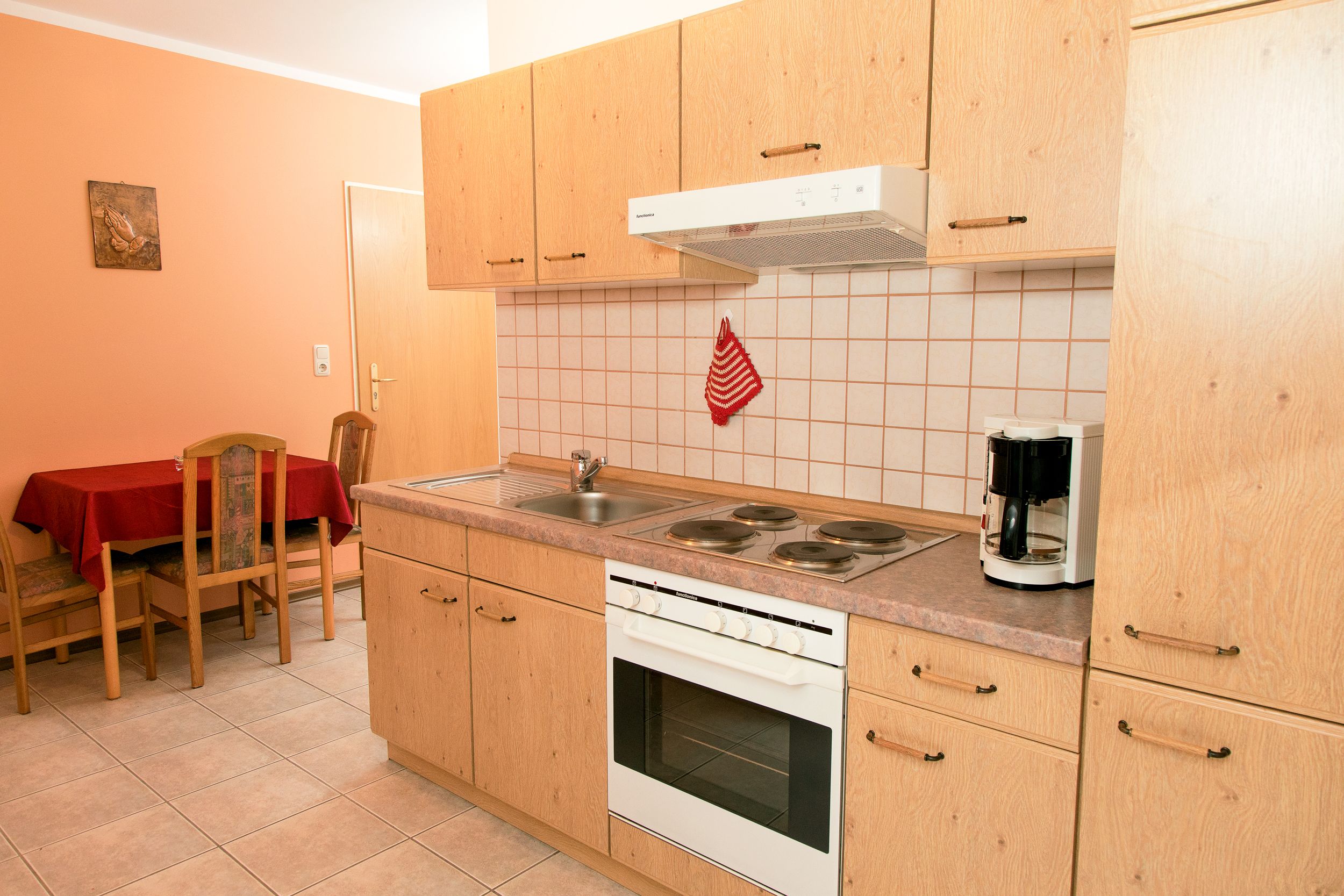 Una cocina con armarios de madera, una estufa, una cafetera y una mesa de comedor con sillas.