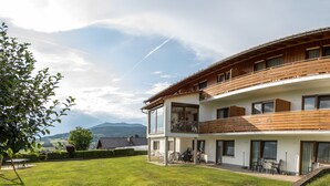 A two-story building with a balcony, a lawn, and a mountainous backdrop. - Appartementhaus Weber (Arrach)