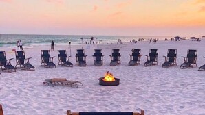 A beach with lounge chairs arranged in rows, a fire pit in the center, and the word 'Surfside' on a chair. - Free Beach Svc=2 Chairs/1 Umbrella! Awesome Views! Free Beach Bonfires M/F nts (Miramar Beach)