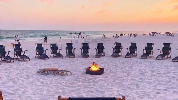 A beach with lounge chairs arranged in rows, a fire pit in the center, and the word 'Surfside' on a chair.