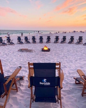 Une plage avec des chaises longues disposées en rangées, un foyer au centre et le mot « Surfside » écrit sur une chaise.