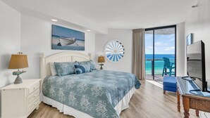 A bedroom with a bed, a painting, a dartboard, a TV, and a view of the sea.