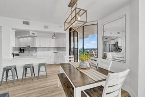 Une cuisine moderne avec des meubles blancs, une table à manger en bois et une vue sur l’extérieur.