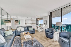 Ein modernes Wohnzimmer mit einer Couch, Couchtisch und Sesseln, ein Essbereich mit Tisch und Stühlen sowie eine Küche mit weißen Schränken.