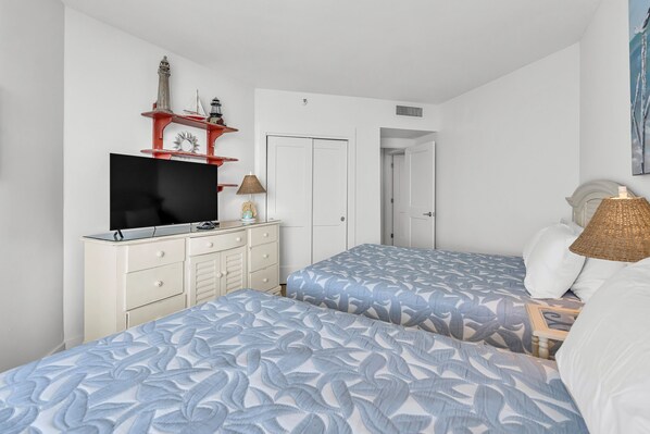 Un dormitorio con dos camas, un televisor, un armario y una puerta que da a otra habitación.