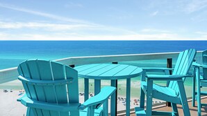 A deck with turquoise Adirondack chairs and a table overlooking a beach with clear blue water.