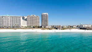 Ein Strandhotel mit mehreren Hochhäusern, einem Sandstrand und klarem, blauem Wasser.