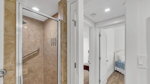 A modern bathroom with a glass shower enclosure, a visible showerhead, and a handrail.