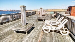 A wooden deck with lounge chairs and a pool table, overlooking a body of water and buildings.