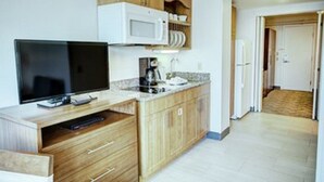 A compact kitchen with wooden cabinets, a microwave, a sink, and a television.