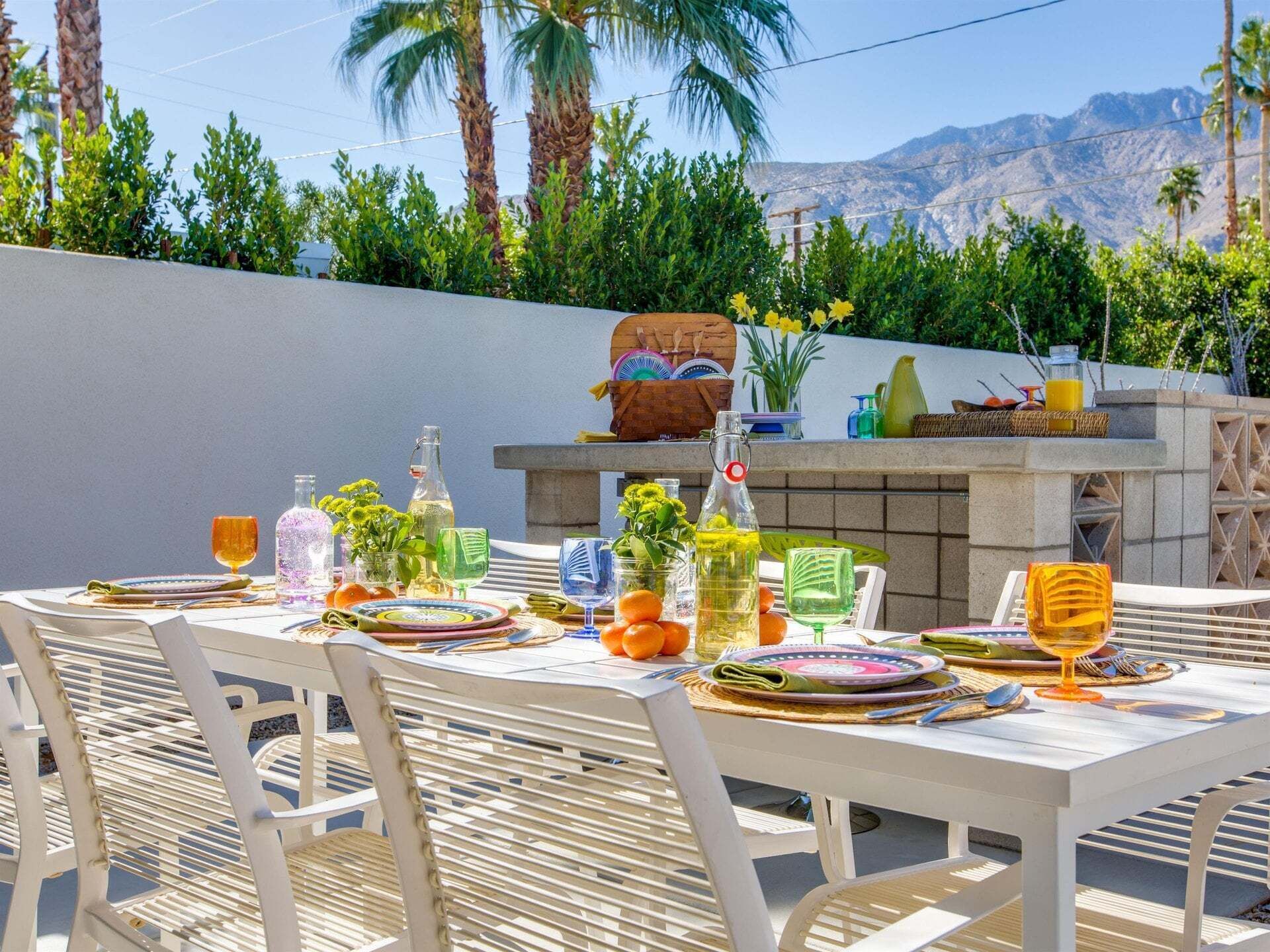 An outdoor dining area with a table set for four, surrounded by chairs, and a barbecue grill in the background.