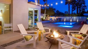 An outdoor pool area with lounge chairs, a fire pit, and string lights.