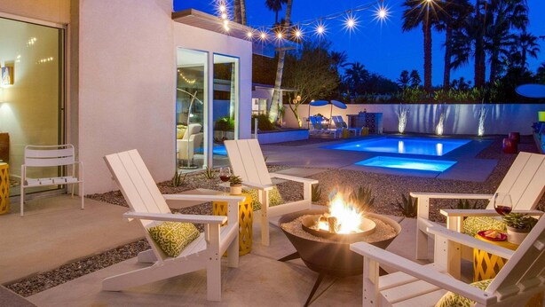 Un área de piscina al aire libre con sillones de descanso, una chimenea y luces colgantes.