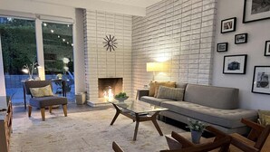 Una sala de estar moderna con chimenea, un sofá, una mesa de centro y sillones de mimbre.