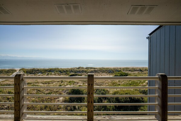A view from a covered area with a railing, overlooking a beach and ocean.