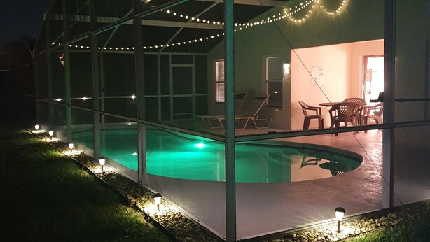 Une piscine extérieure couverte, protégée par une structure en verre, entourée d’une terrasse agrémentée de guirlandes lumineuses.