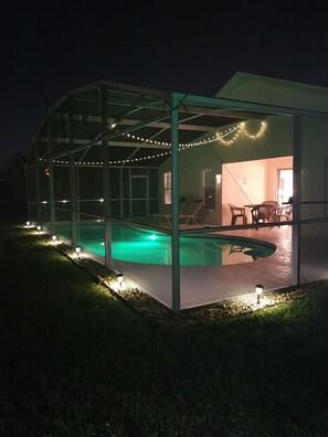 Une piscine extérieure couverte, protégée par une structure en verre, entourée d’une terrasse agrémentée de guirlandes lumineuses.