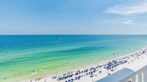 Una playa con agua turquesa cristalina, arena blanca y numerosas sombrillas azules.
