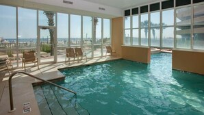 Una piscina interior con vistas despejadas a la playa, rodeada de sillones de descanso y una barrera de cristal.
