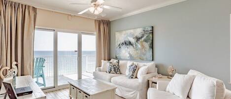 A spacious living area with a balcony, white furniture, and a ceiling fan.