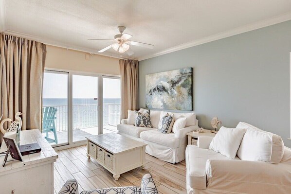 A spacious living area with a balcony, white furniture, and a ceiling fan. - Seawind 1409 | Gulf Shores, AL (Gulf Shores)