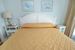 A neatly made bed with a quilted cover, a bedside table with a lamp, and two framed pictures on the wall. - Oceanfront Views from Every Room in This Condo (Myrtle Beach)
