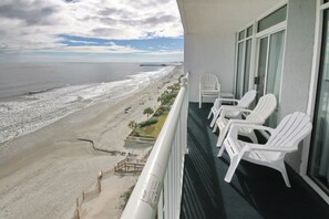 A balcony with white chairs overlooking a beach with a pier in the distance. - Oceanfront Views from Every Room in This Condo (Myrtle Beach)