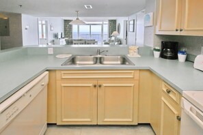 A modern kitchen with a double sink, wooden cabinets, and a view to the living area. - Oceanfront Views from Every Room in This Condo (Myrtle Beach)